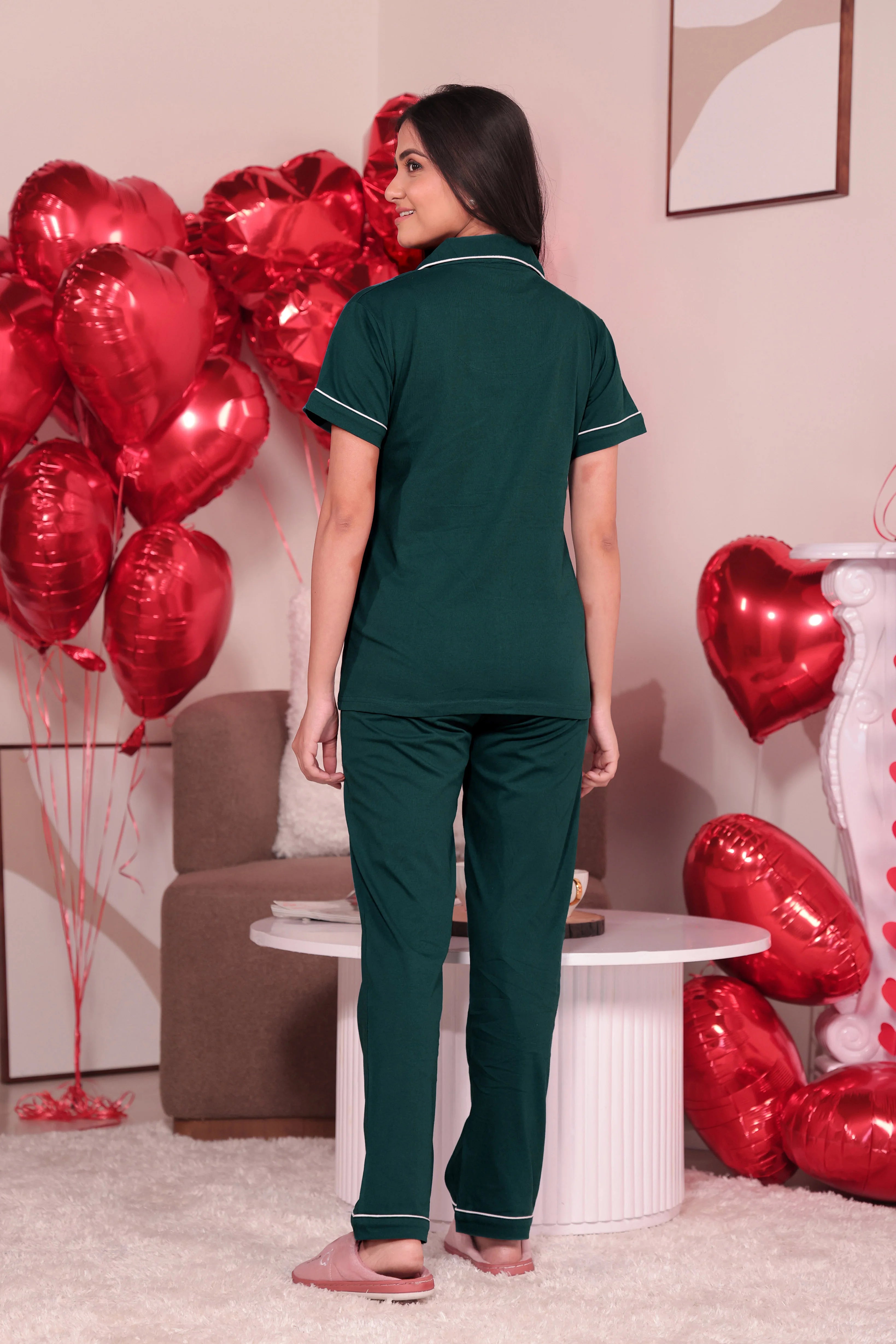 Rear view of woman standing in dark green short sleeve pajama set with tapered pants and pink slippers. Casual and cozy nightwear.