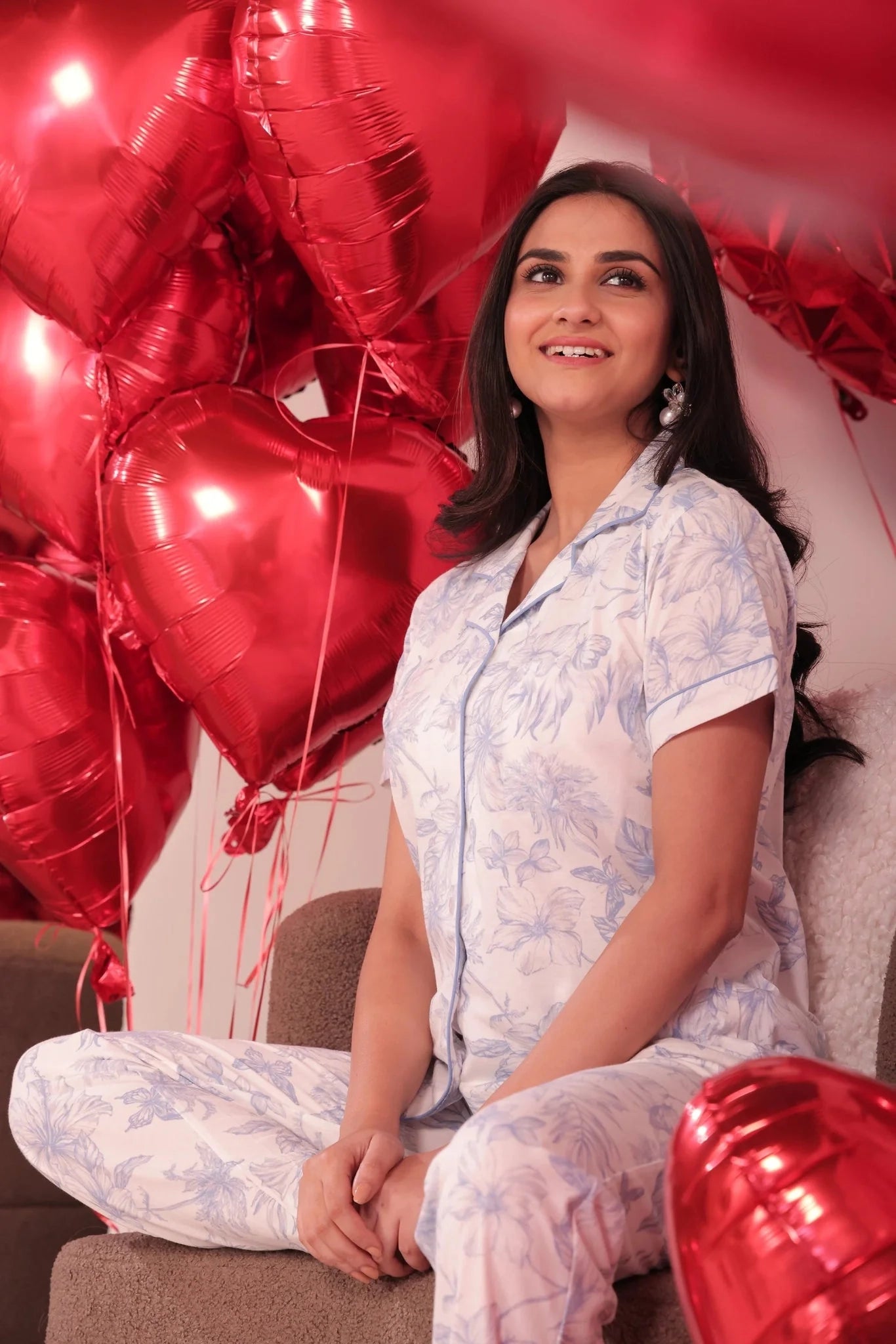 Woman in pajamas sitting among red heart-shaped balloons