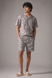 Man wearing a gray floral shirt and shorts set against a plain background