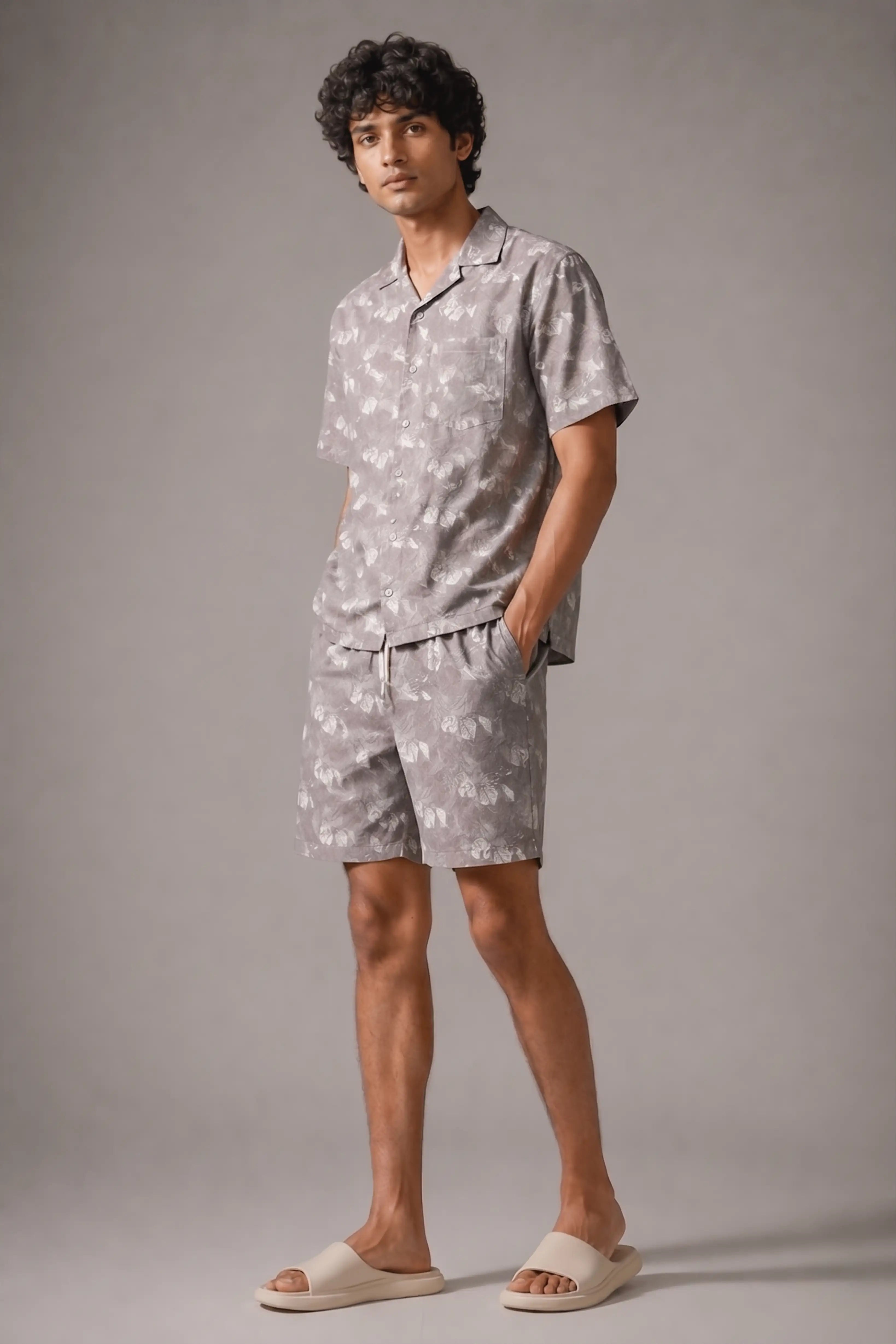 Man wearing a light gray patterned shirt and shorts set against a plain background