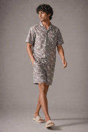 Man wearing a gray patterned shirt and shorts on a gray background