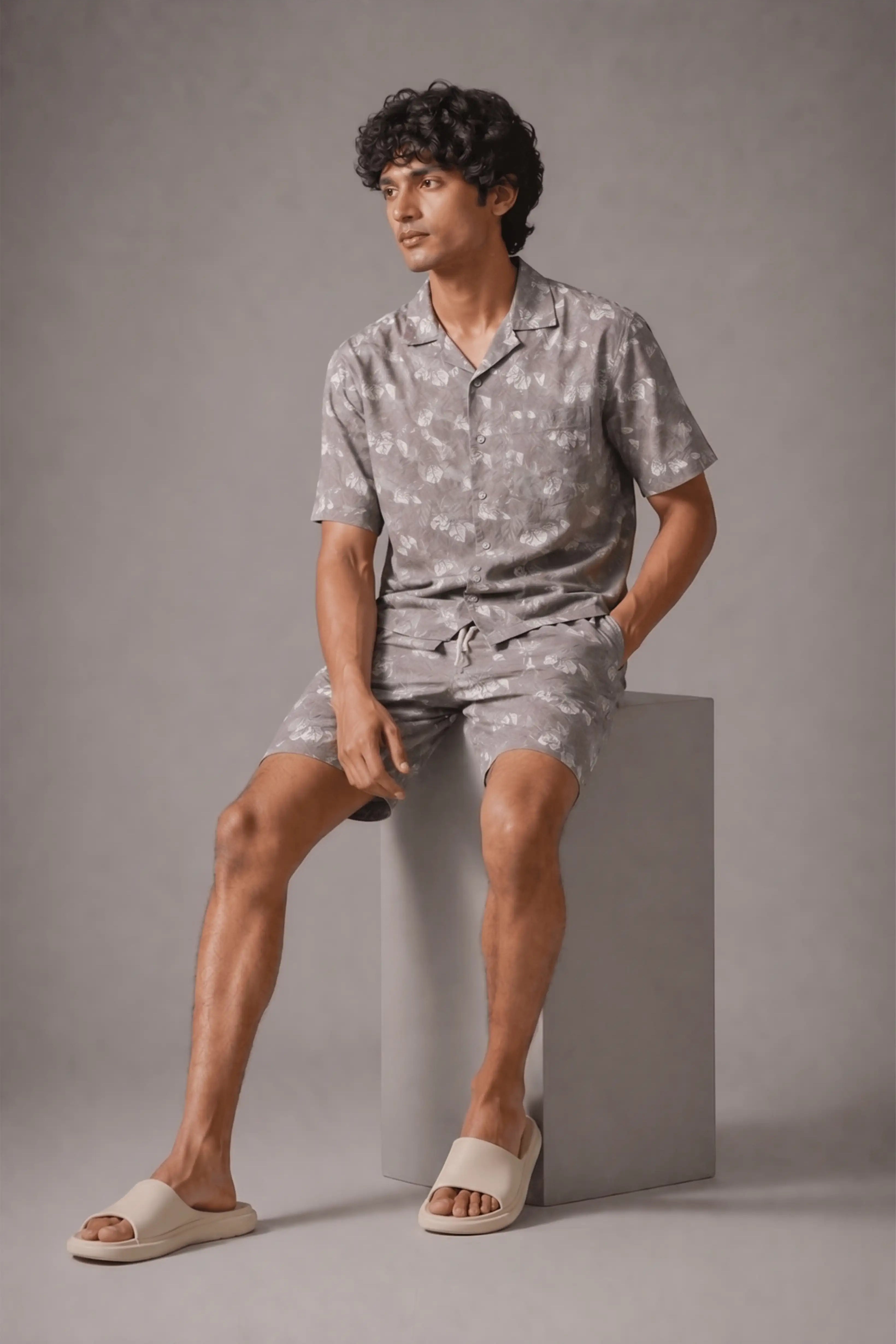 Man wearing a gray floral pajama set sitting on a gray block against a gray background