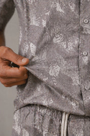 Close-up of a person wearing a gray floral patterned shirt and pants.