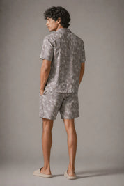 Man wearing a gray patterned shirt and shorts set against a plain background