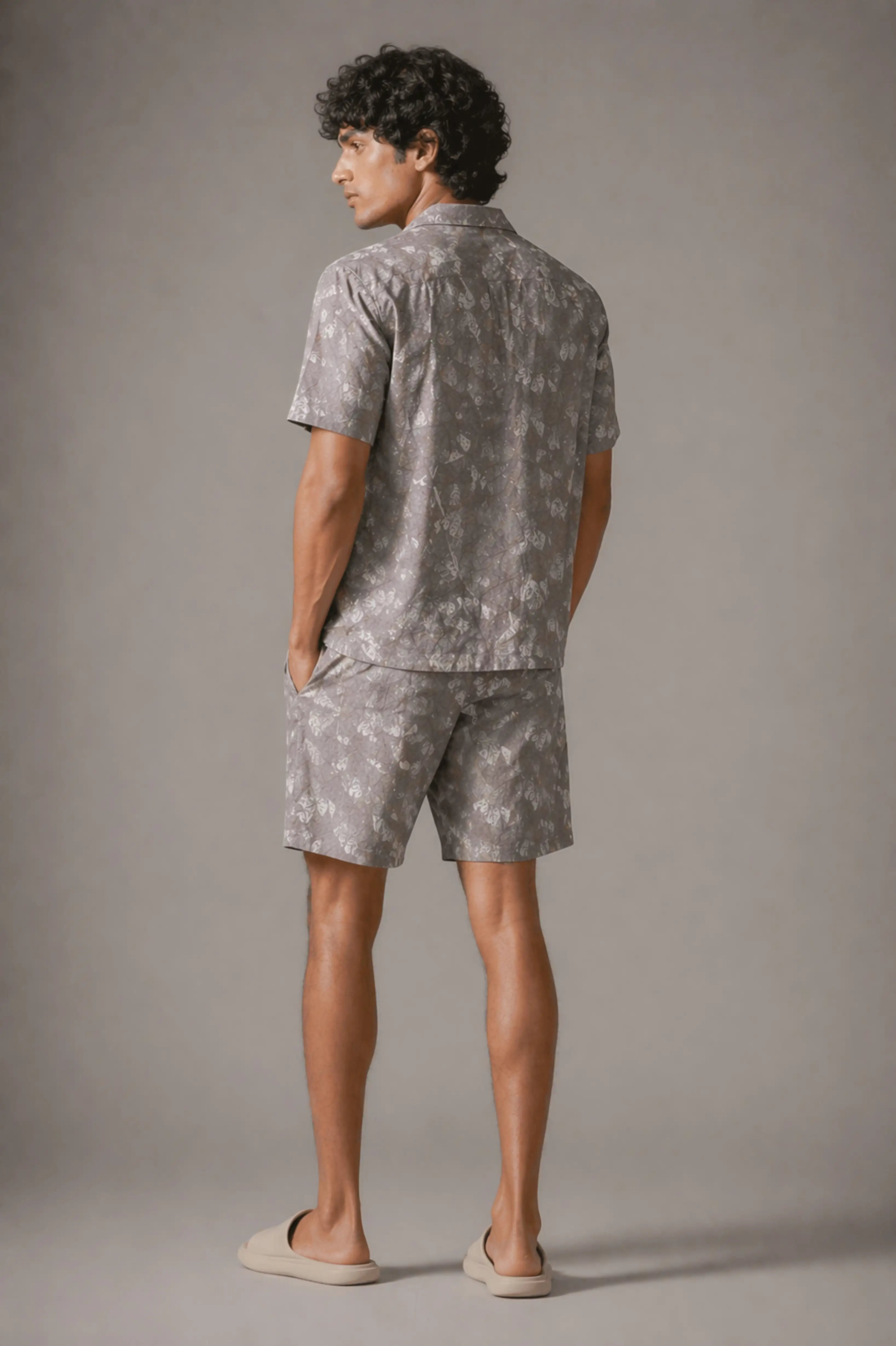 Man wearing a gray patterned shirt and shorts set against a plain background