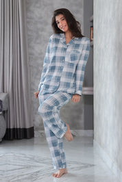 A woman wearing blue plaid pajamas standing in a room with gray walls and a marble floor.