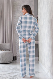 A woman wearing blue and white plaid pajamas in a room with curtains and a chair.