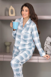 Woman wearing blue plaid pajamas holding a blue mug in a home setting.