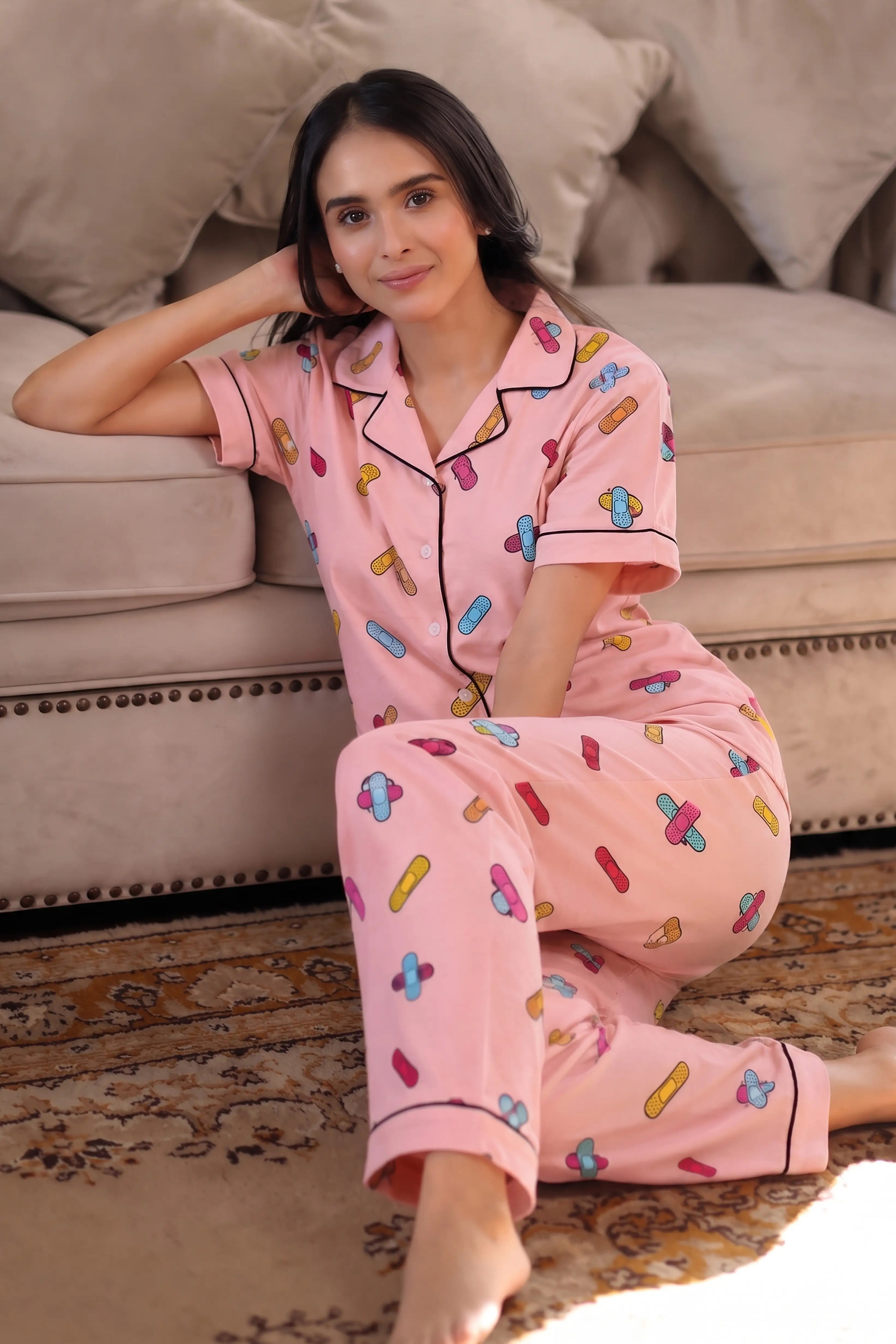 Woman wearing pink pajamas with colorful patterns sitting on a couch.