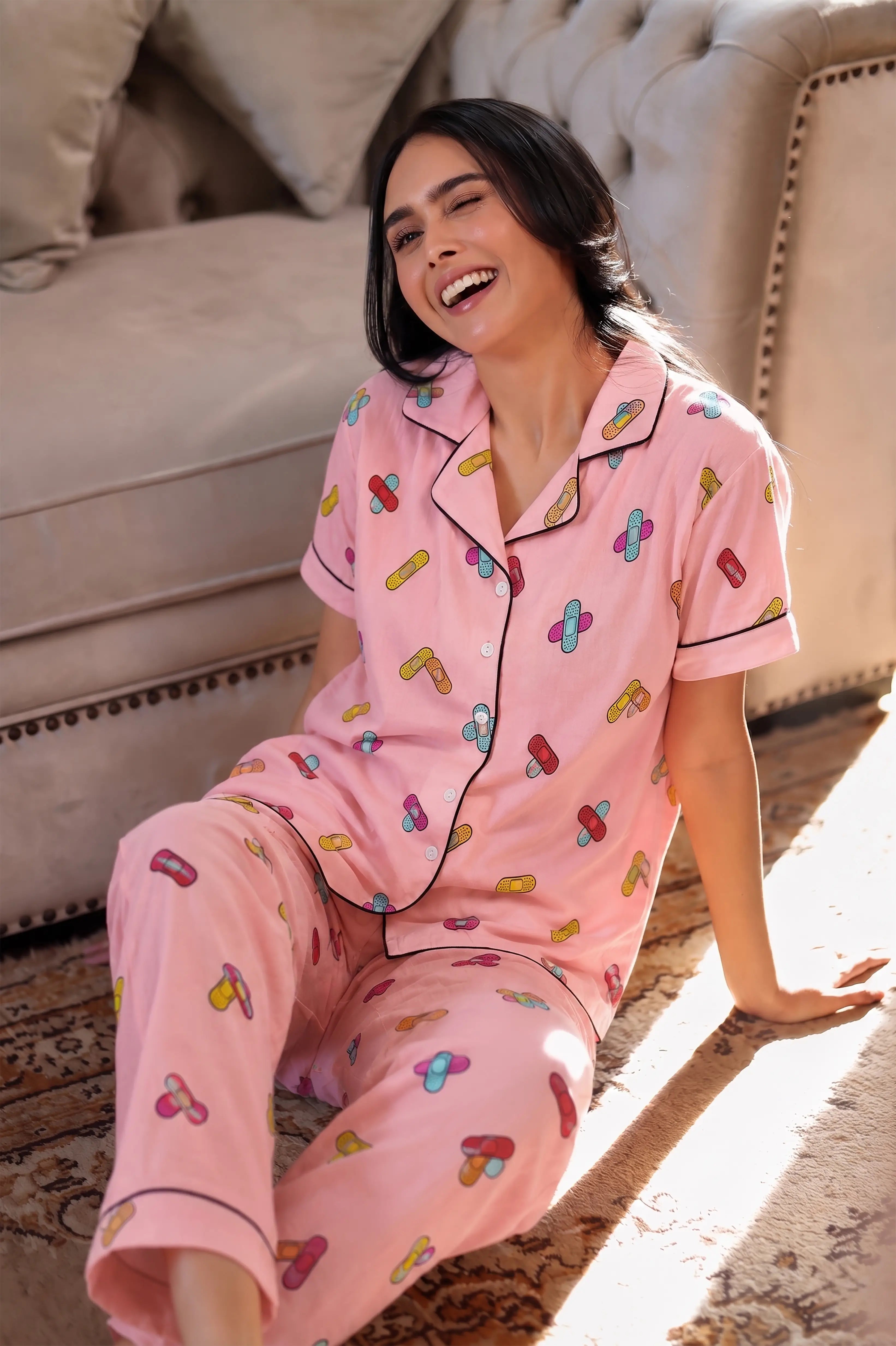 Woman wearing pink pajamas with colorful patterns sitting on a couch.