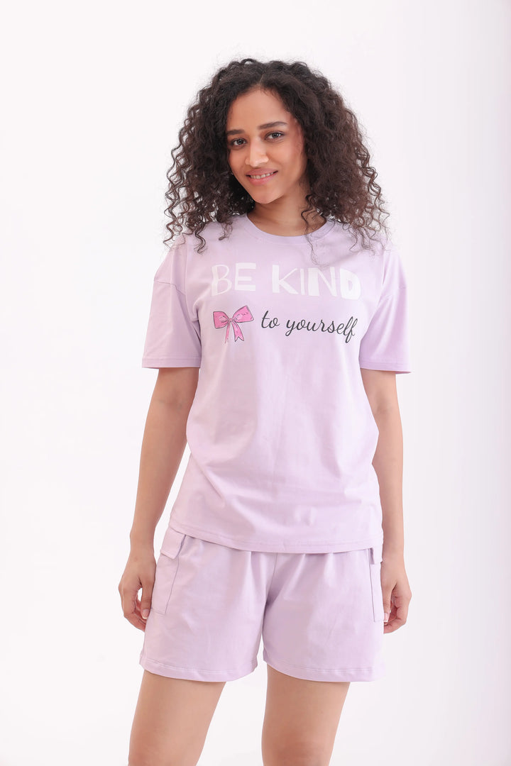 Woman in lavender oversize t-shirt & cotton shorts, smiling softly, relaxed nightwear by NapStory.