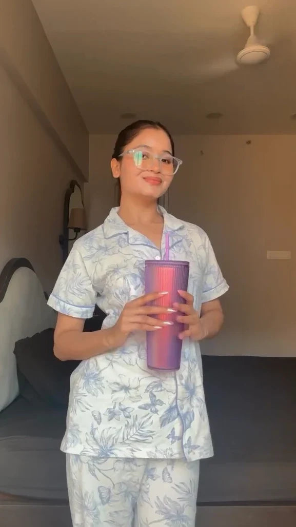 Person wearing a light blue pajama set holding a purple tumbler with a straw in a room.