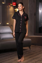 A woman wearing a black pajama set with Pink piping in a room.
