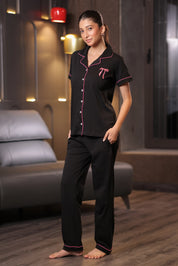 Woman wearing a black bow embroidery pajama set with pink accents in a room.