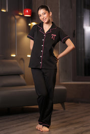 Woman wearing a black pajama set with pink accents in a dimly lit room.