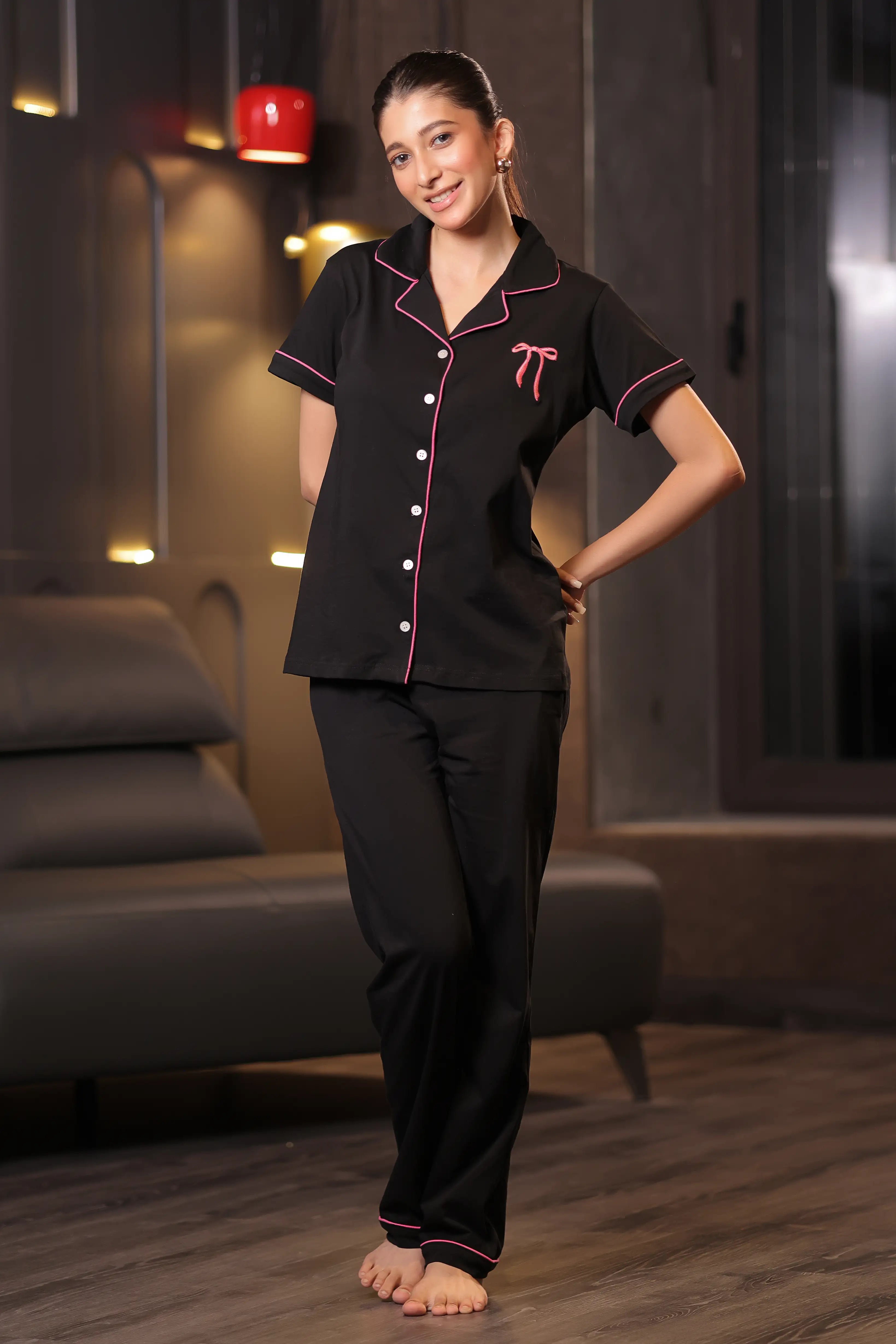 Woman wearing a black pajama set with pink accents in a dimly lit room.