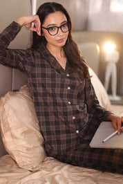 Woman in plaid pajamas sitting on a bed with a notebook and pen.