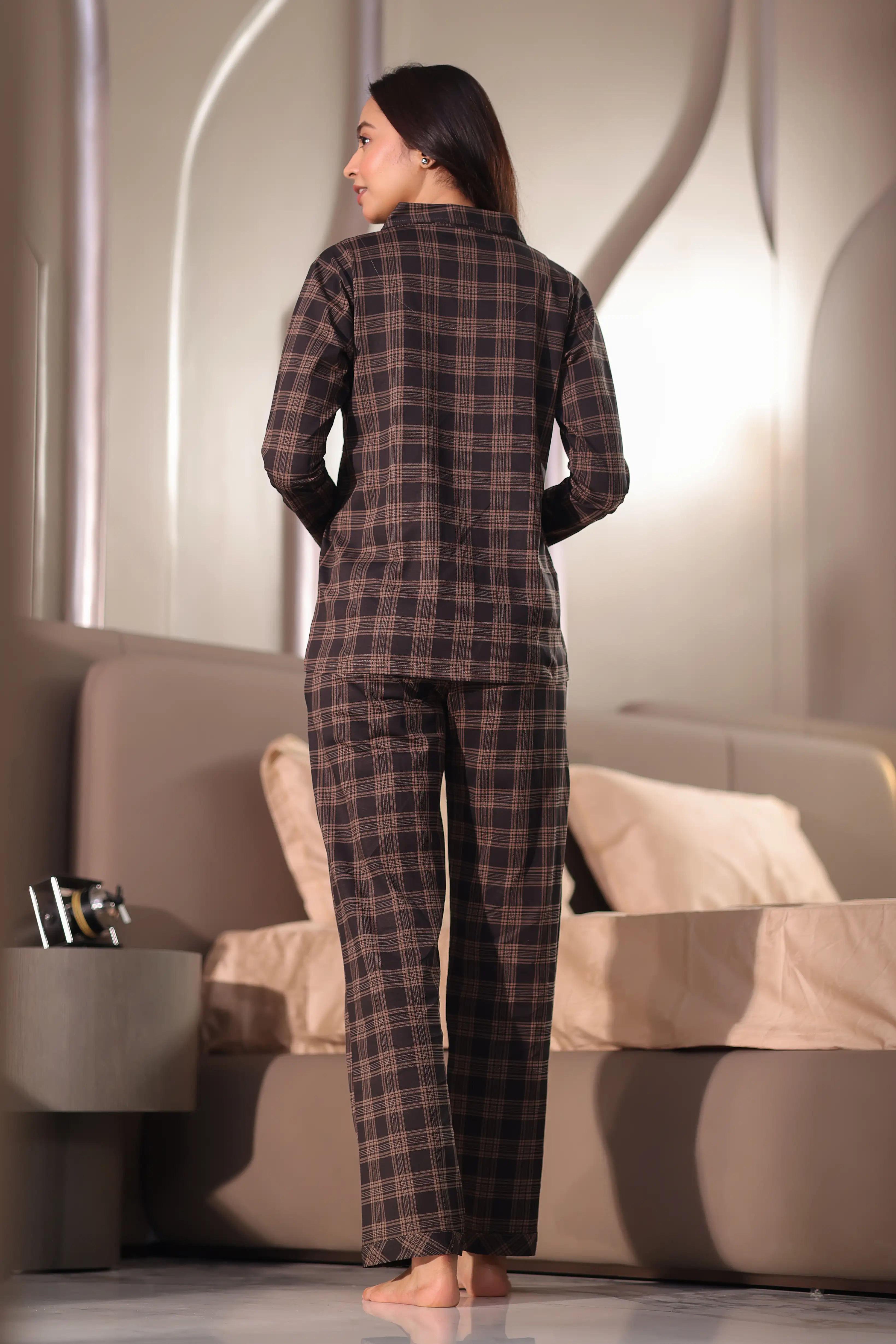 Woman wearing a plaid pajama set in a modern bedroom.