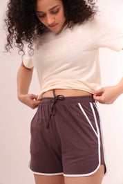 Woman adjusting brown piped-up shorts, cotton loungewear by NapStory
