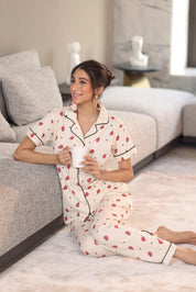 Woman in a patterned pajama set sitting on a couch holding a mug.