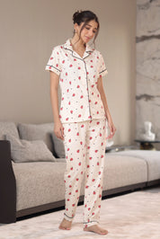 Woman wearing a cream-colored pajama set with red patterns in a living room.