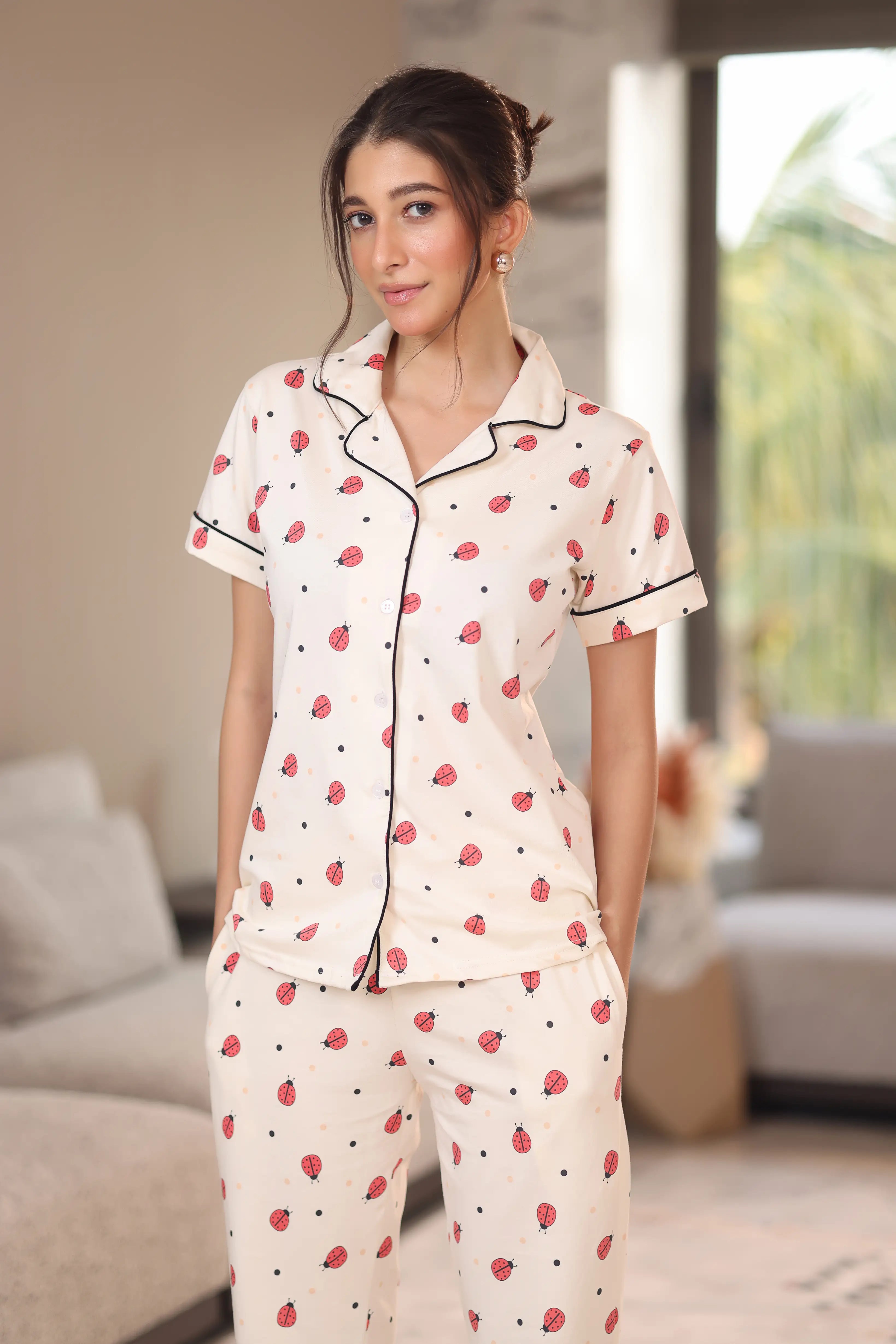 Woman wearing a white pajama set with red patterns in a living room.
