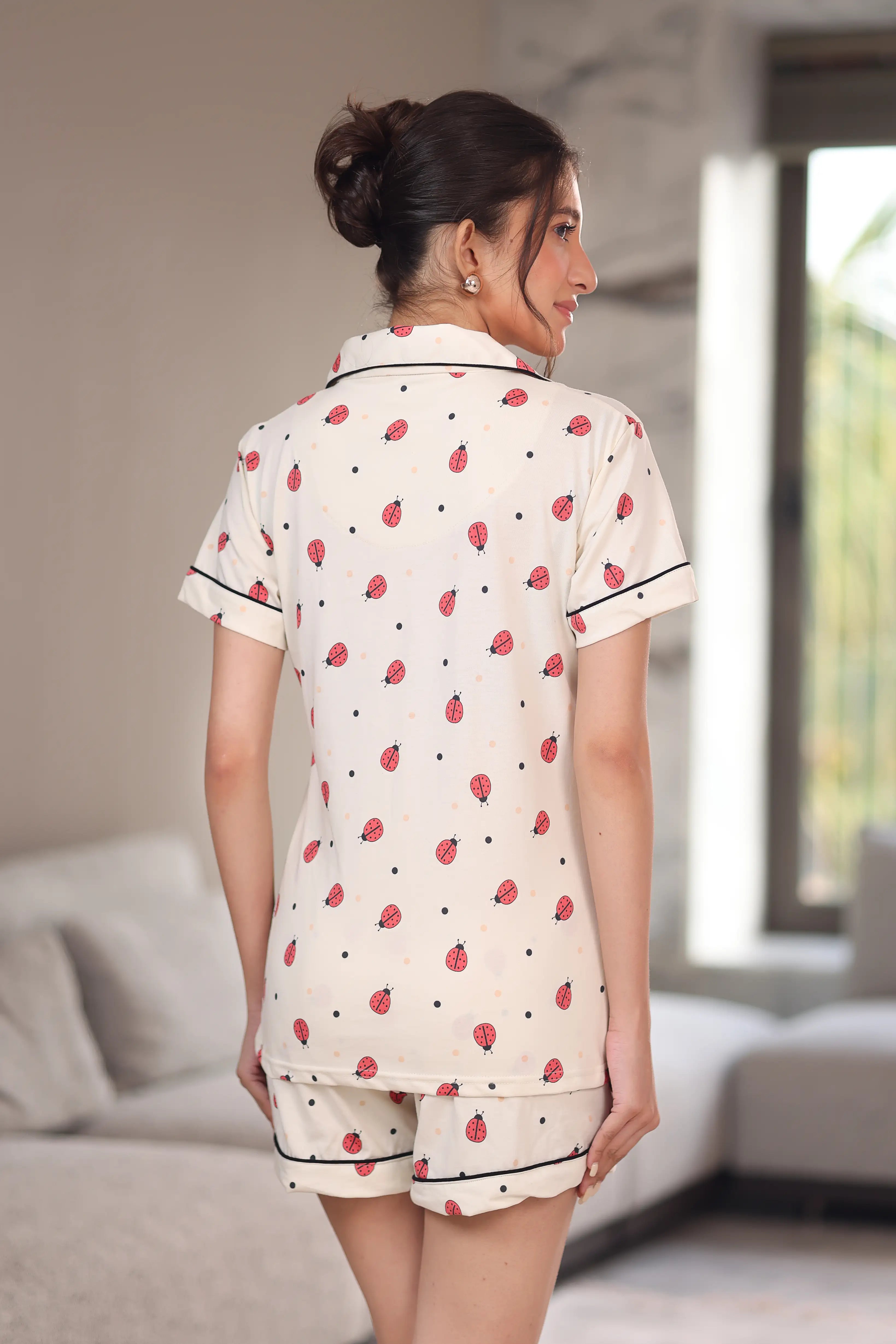 Woman wearing a white printed shorts set with bug and dot patterns in a room.
