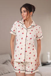 Woman wearing a white printed shorts set with bug patterns in a bedroom setting.