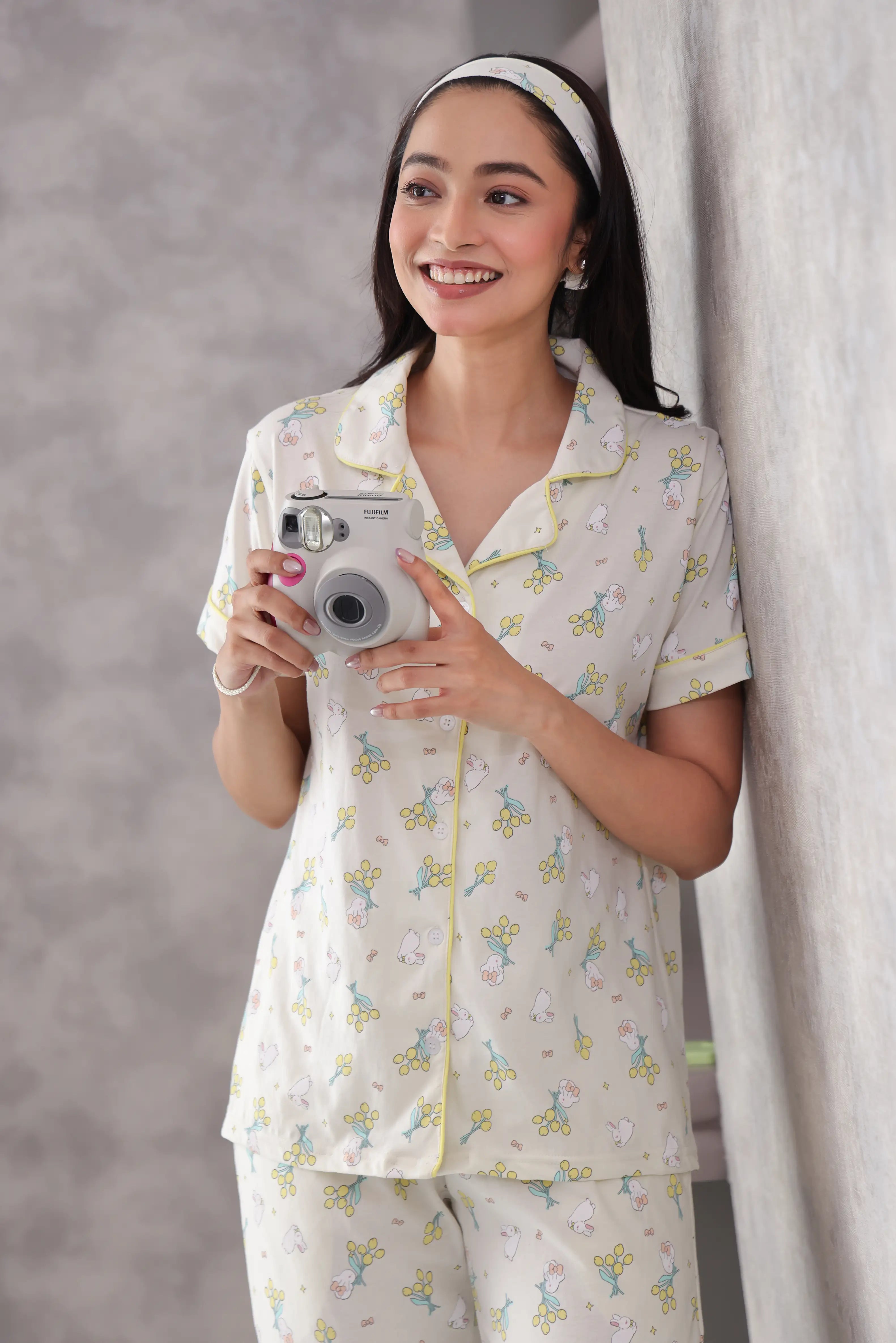 Woman in a bunny printed pajama set holding a camera against a neutral background