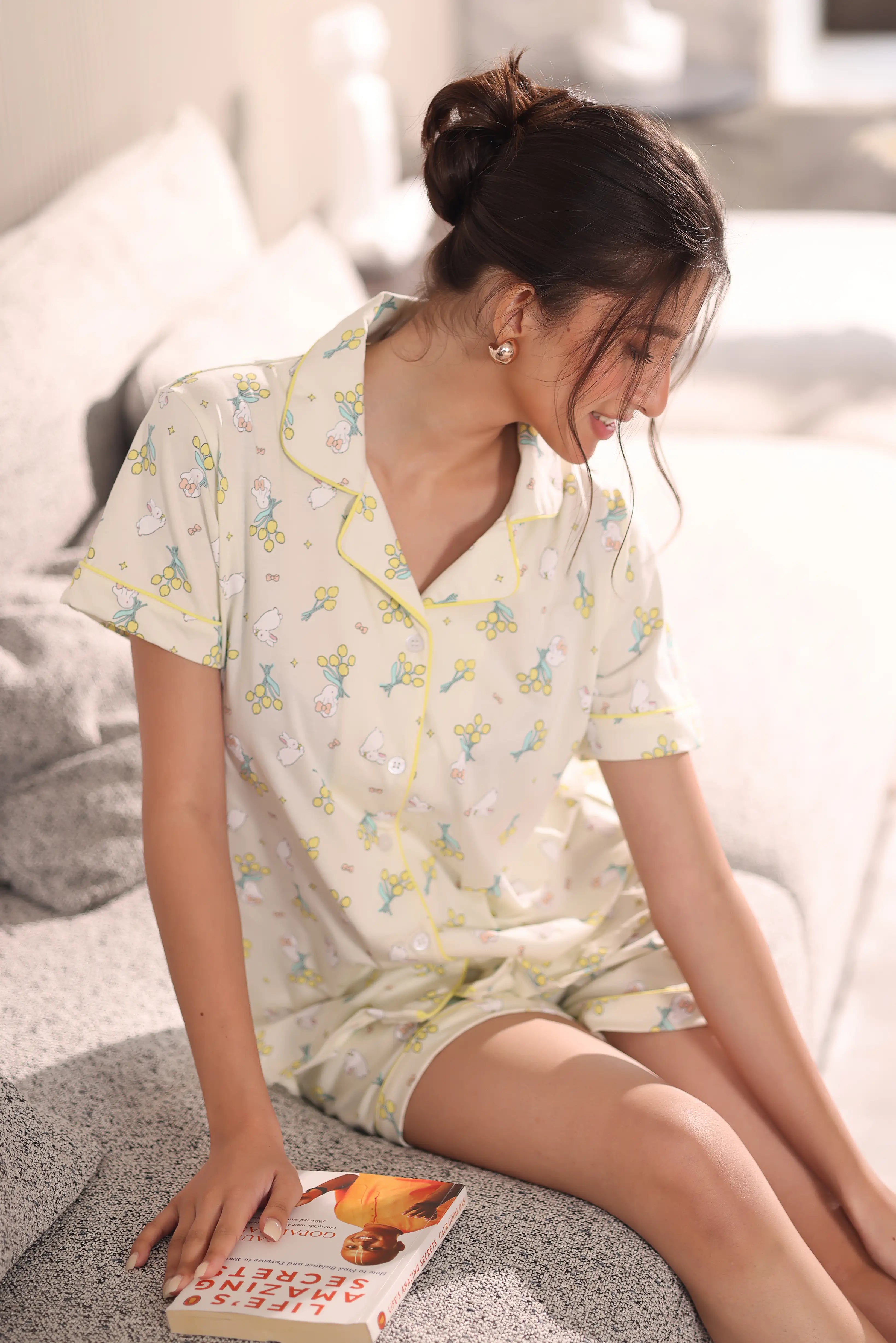 Woman in a bunny print shorts set sitting on a couch with a book.