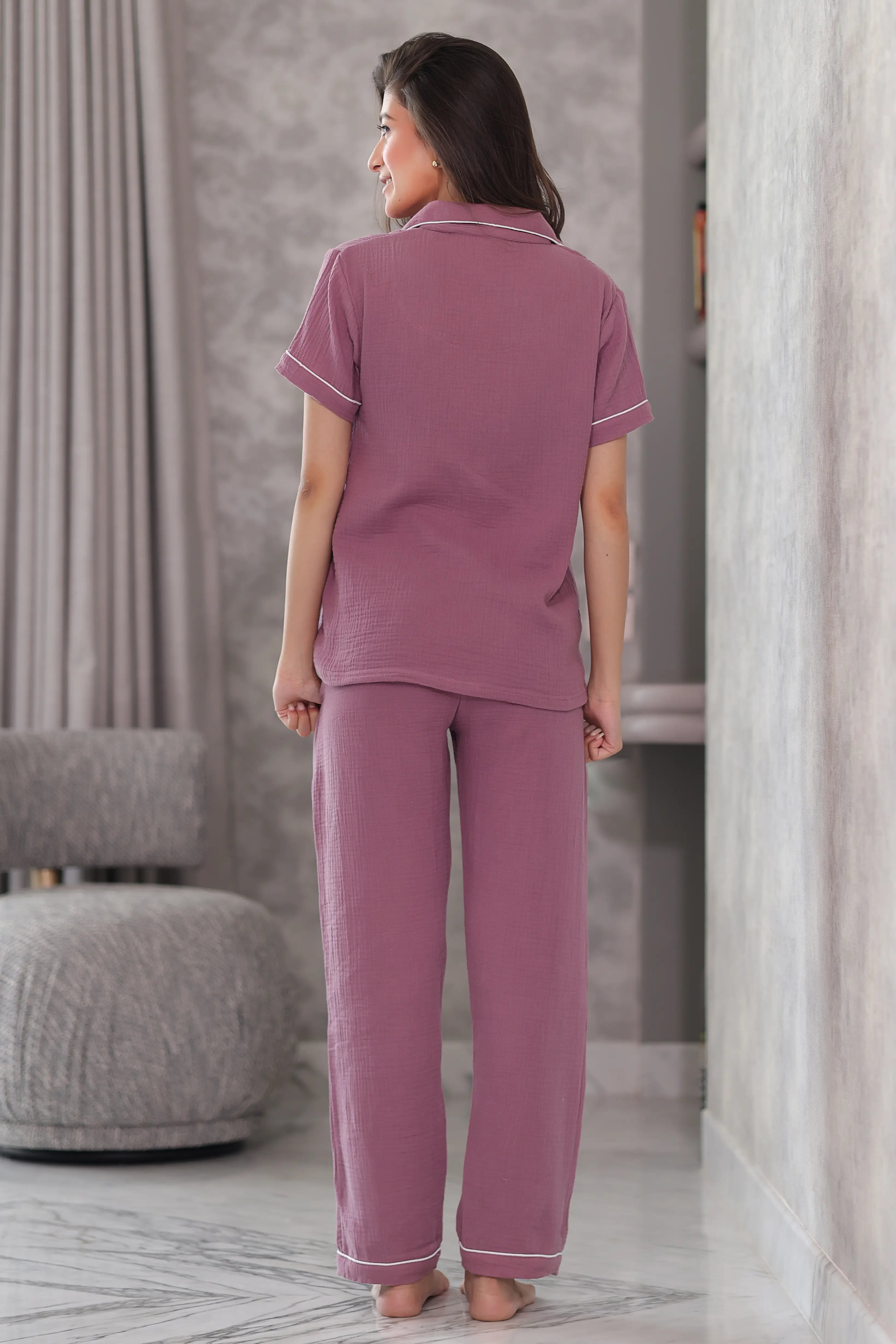 Woman wearing a mauve pajama set in a room with gray curtains and a gray ottoman.