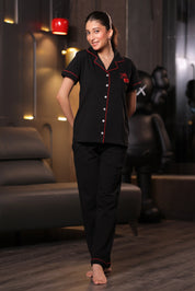 A woman wearing a black embroidered pyjama set with red accents in a room setting