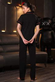 The model is wearing a black embroidery pyjama set with red accents in a dimly lit room.