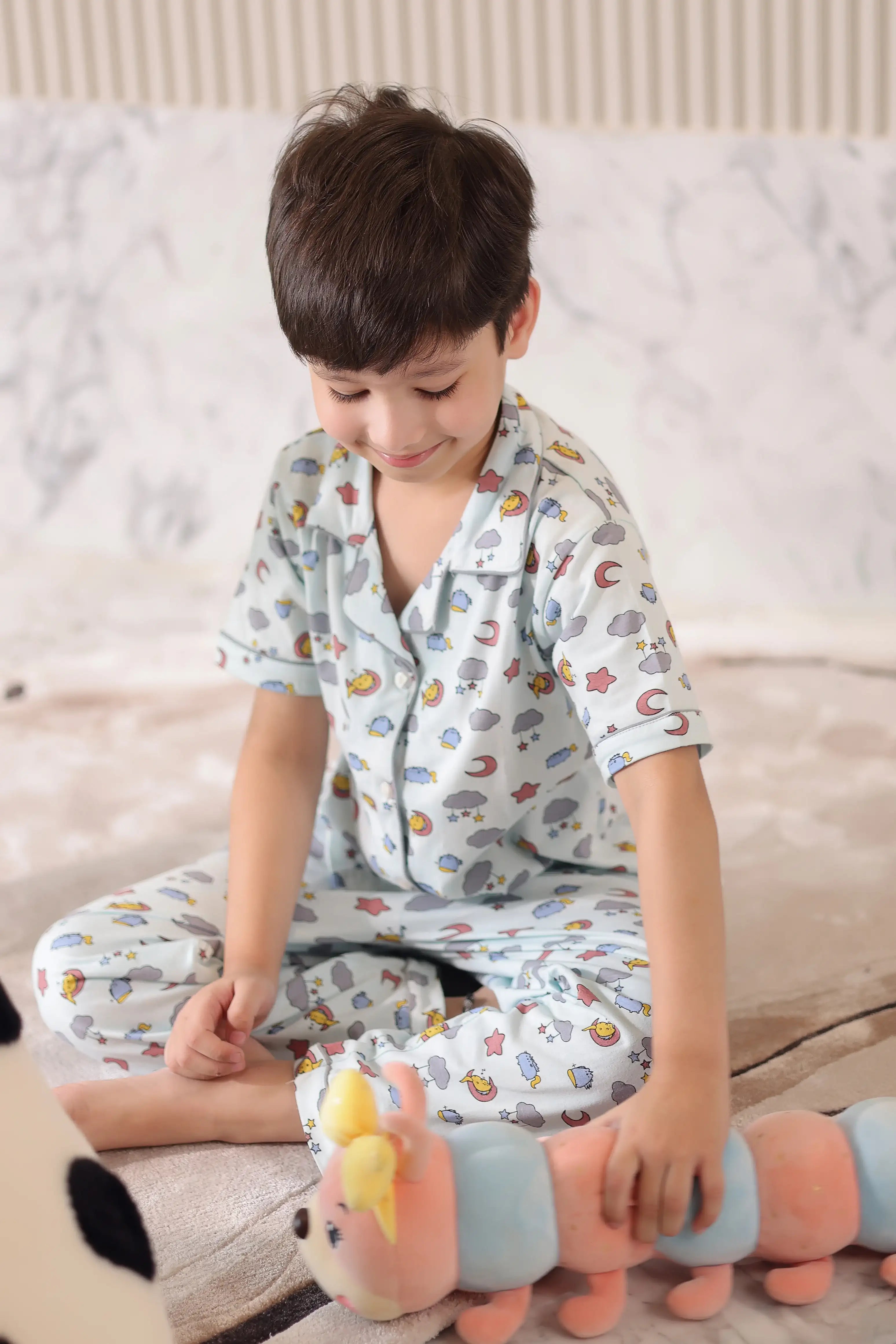 Child wearing pajamas with a pattern of cars and animals, sitting on a couch holding a toy.