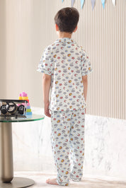Child wearing a cloud-patterned pajama set, standing in a back pose in a room with a table and decorative items.