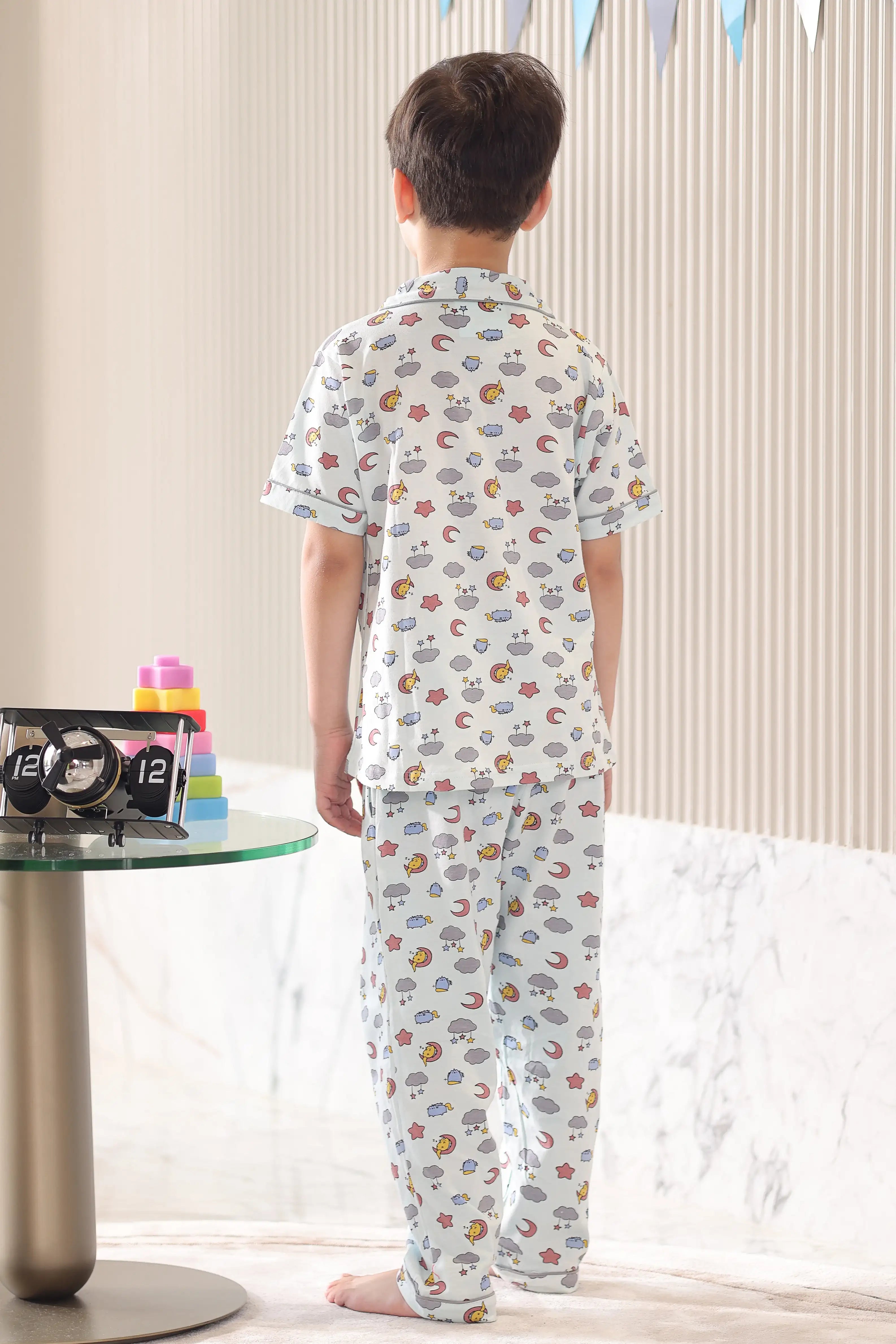 Child wearing a cloud-patterned pajama set, standing in a back pose in a room with a table and decorative items.