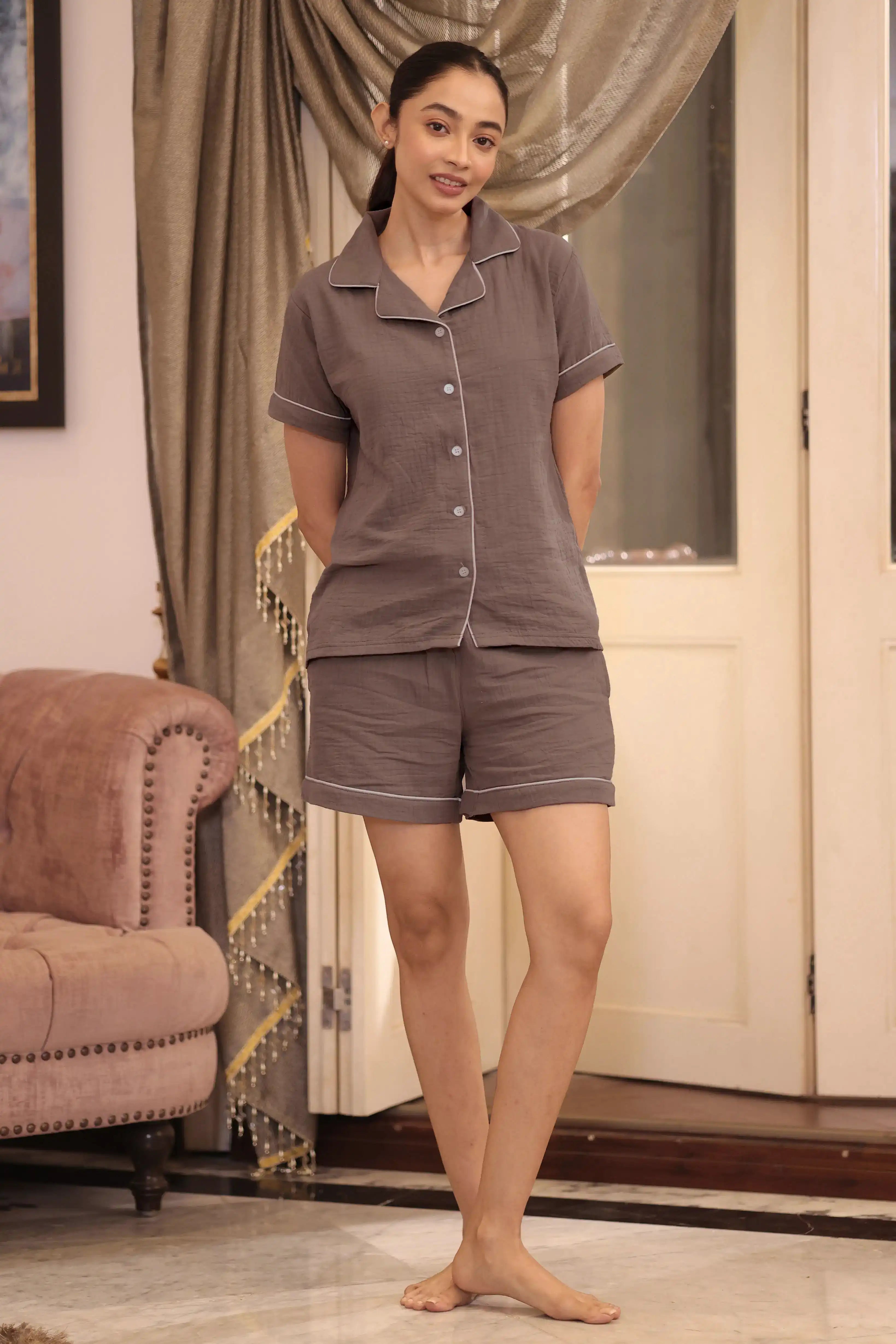 Woman wearing a brown shorts set in a room with a curtain and chair.
