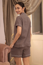 Woman wearing a brown shorts set in a room with curtains and a chair.