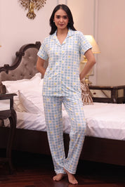 Woman wearing a blue checkered pajama set in a bedroom.