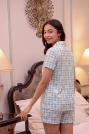 Woman wearing a blue checkered shorts set in a bedroom.