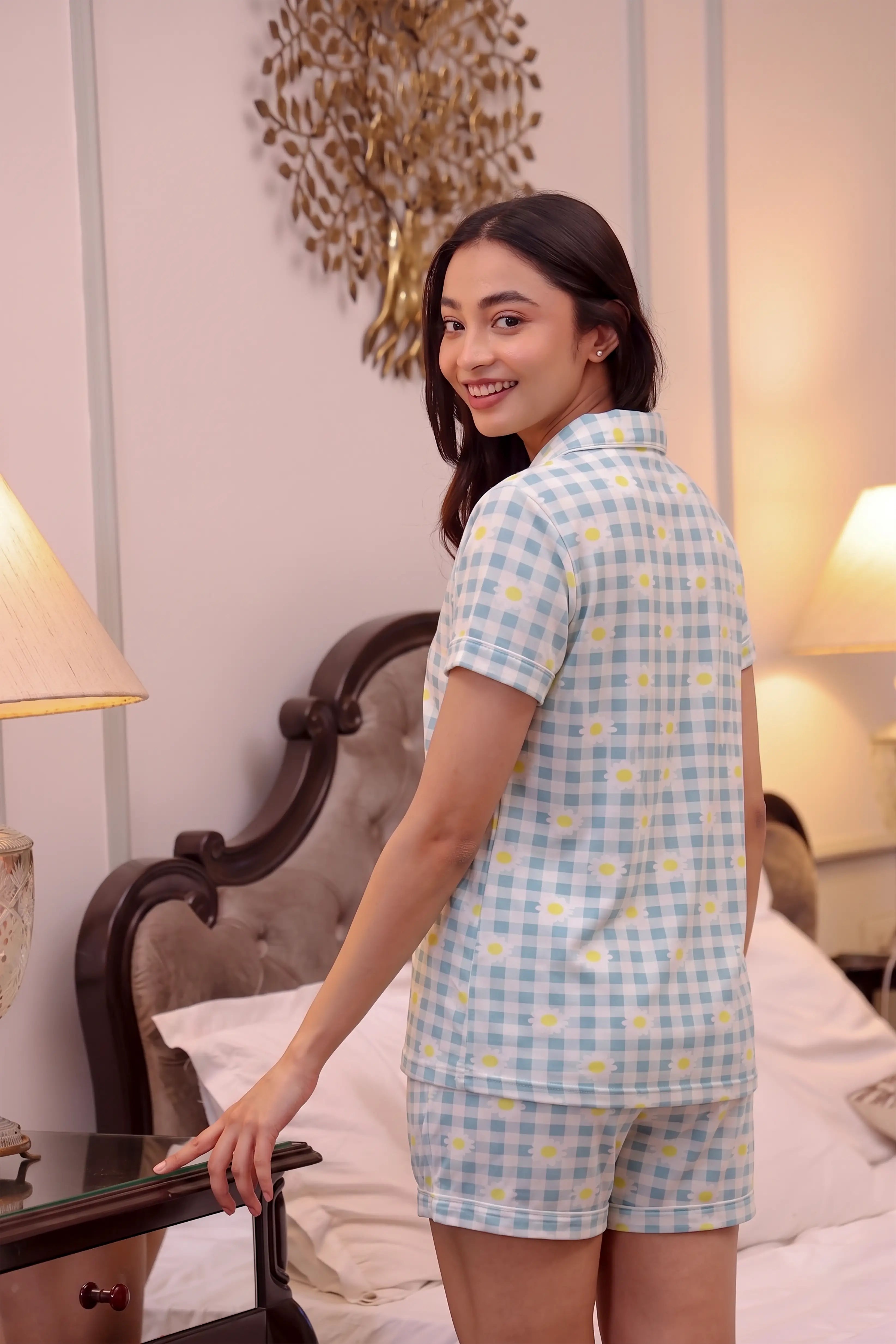 Woman wearing a blue checkered shorts set in a bedroom.