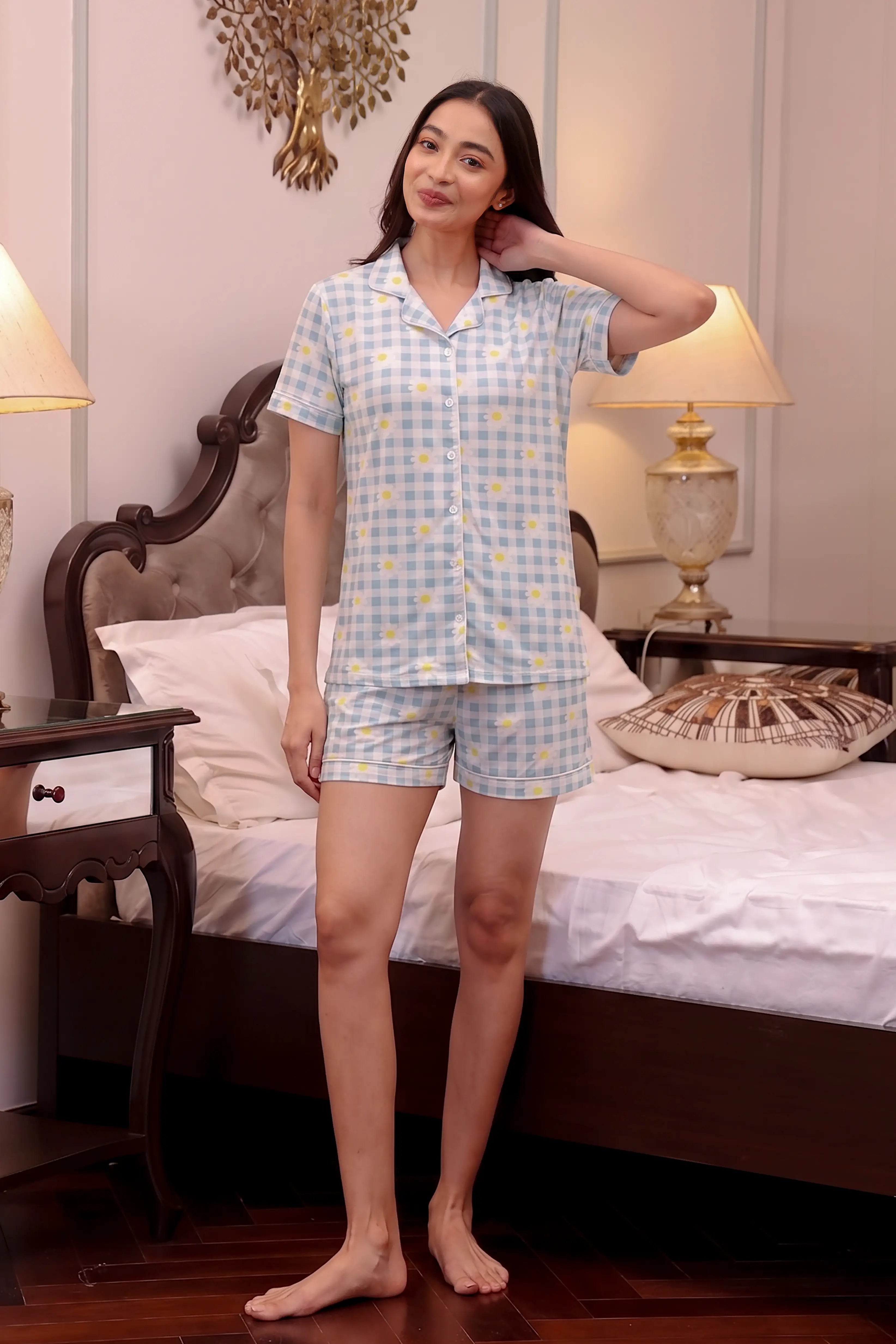 Woman wearing a light blue checkered Shorts set in a bedroom.