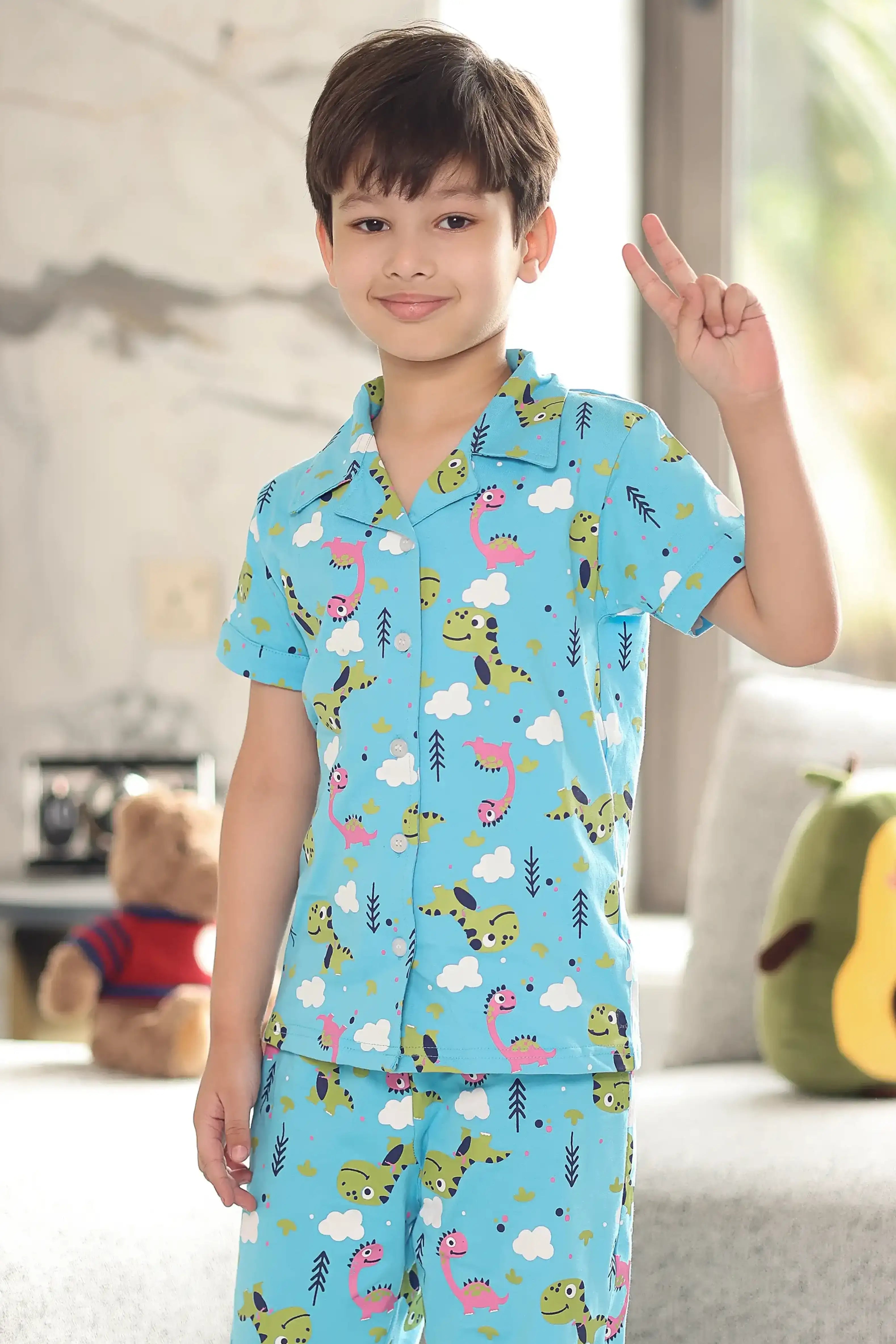 Child wearing a blue pajama set with dinosaur and cloud pattern in a living room.