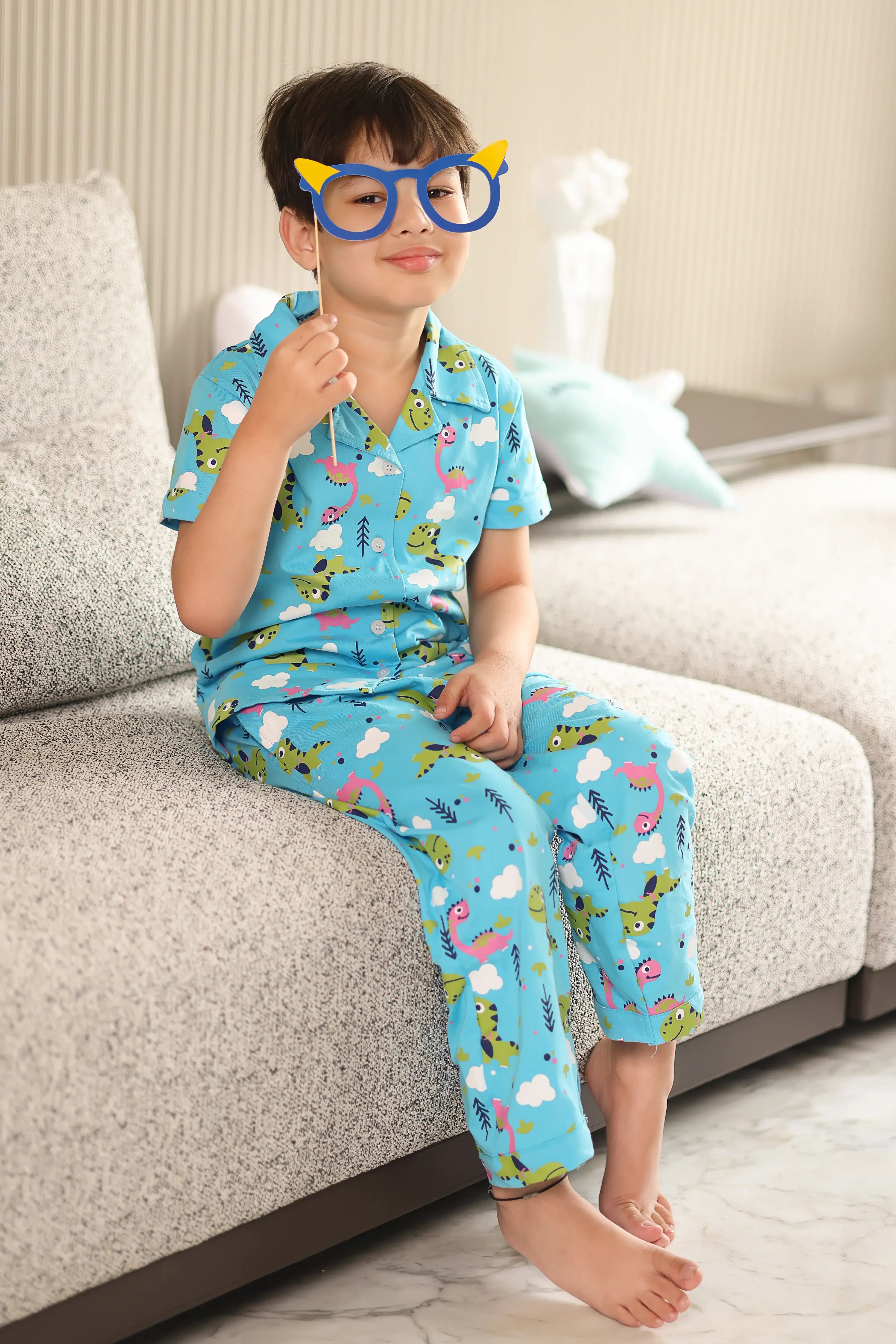A child wearing a blue pajama set with animal prints sitting on a couch.