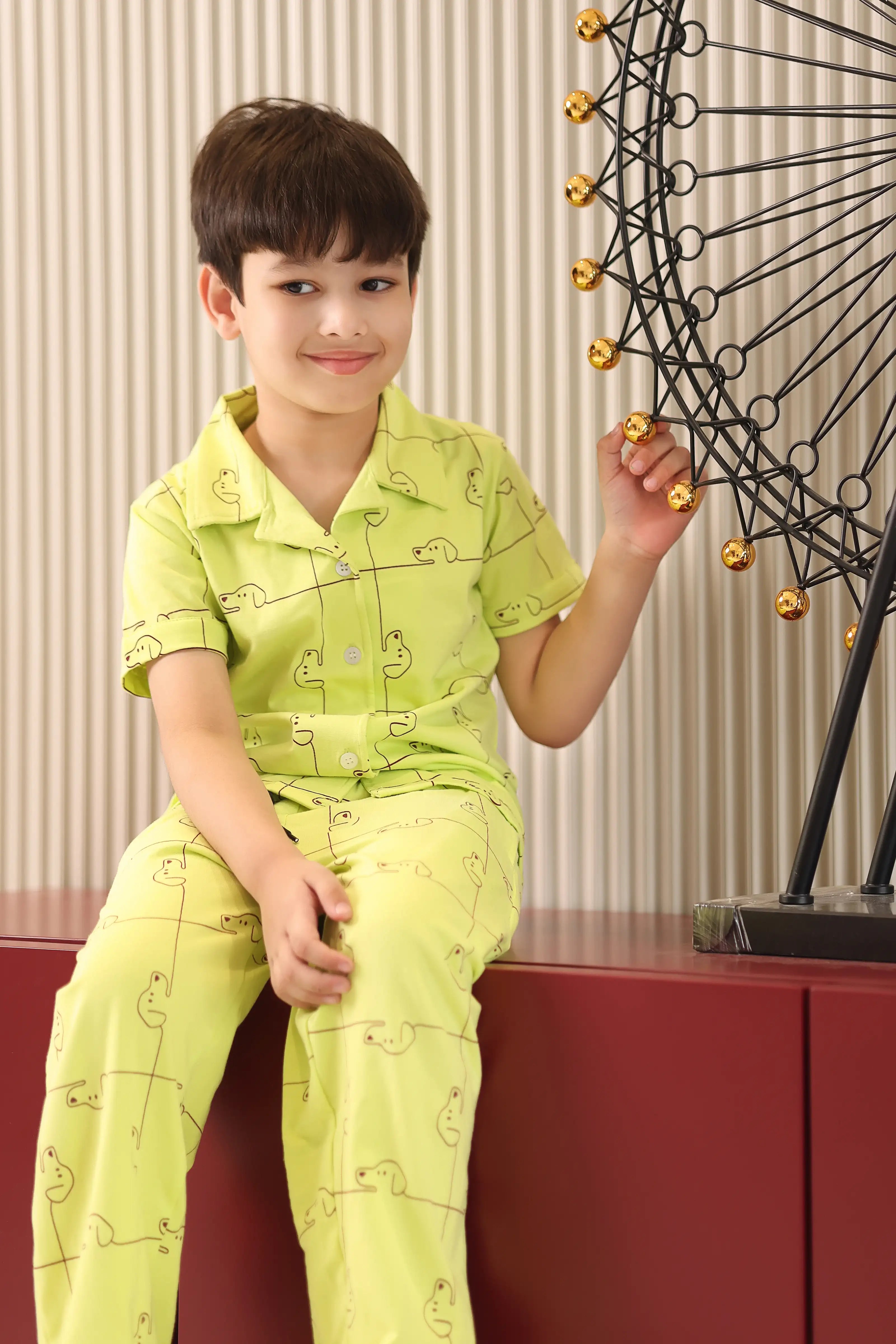 A child wearing a bright green outfit with a dog pattern, sitting on a red surface.