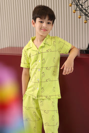 Child wearing a green pajama set with animal patterns, standing against a blurred indoor background.