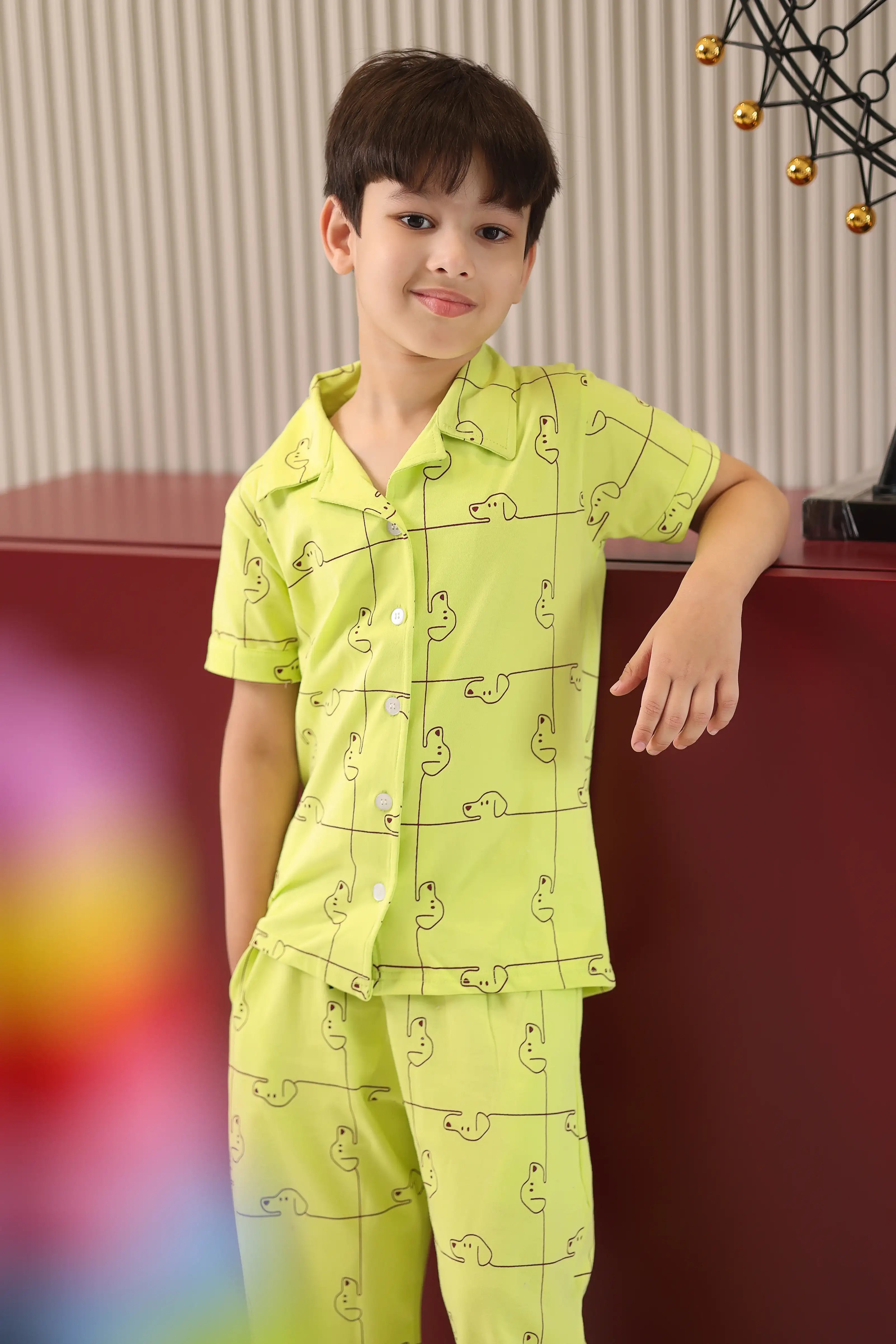 Child wearing a green pajama set with animal patterns, standing against a blurred indoor background.