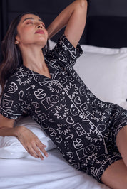 Woman wearing a black patterned outfit lying on a bed.