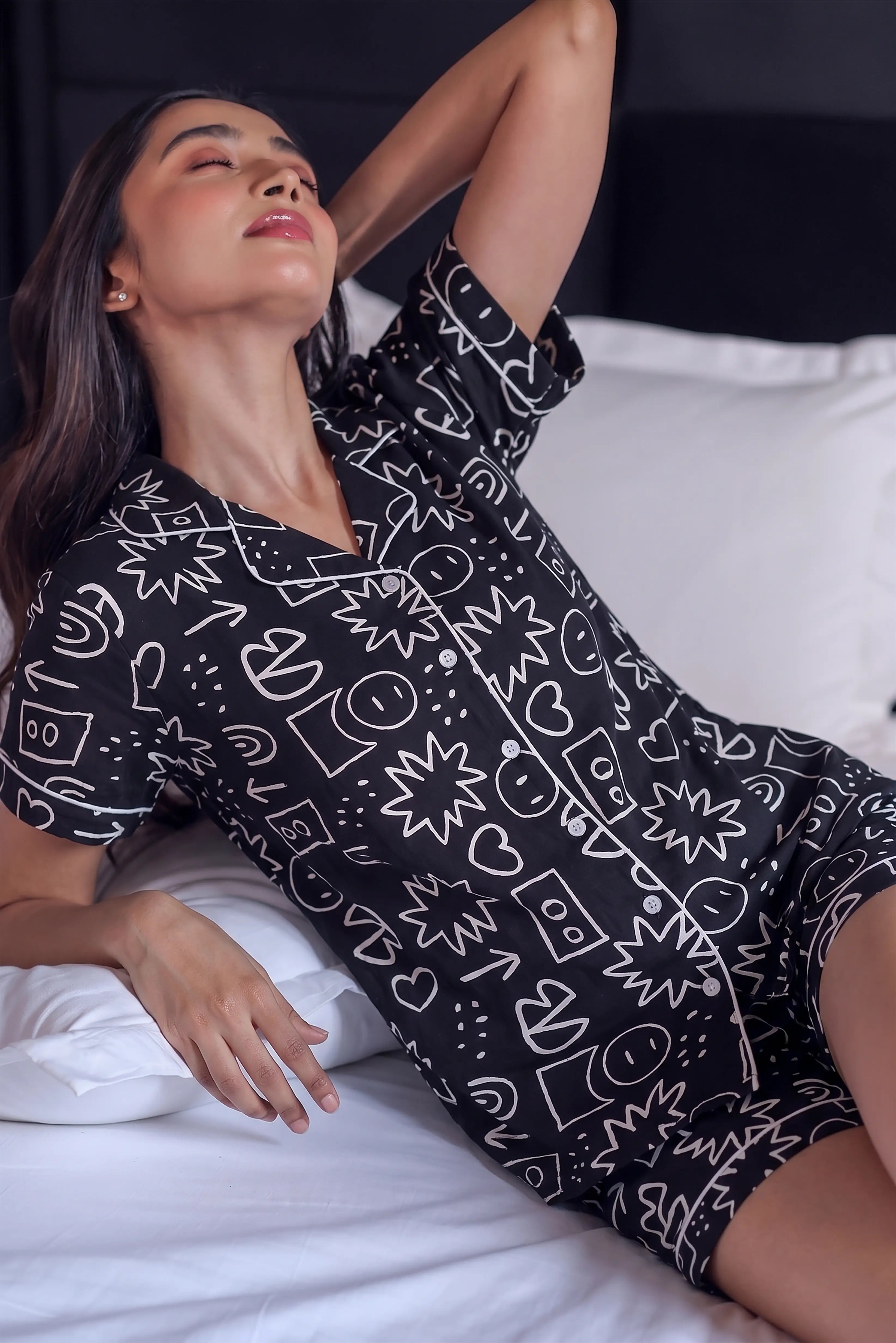 Woman wearing a black patterned outfit lying on a bed.