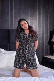 Woman in a patterned shorts set sitting on a bed with decorative wall behind